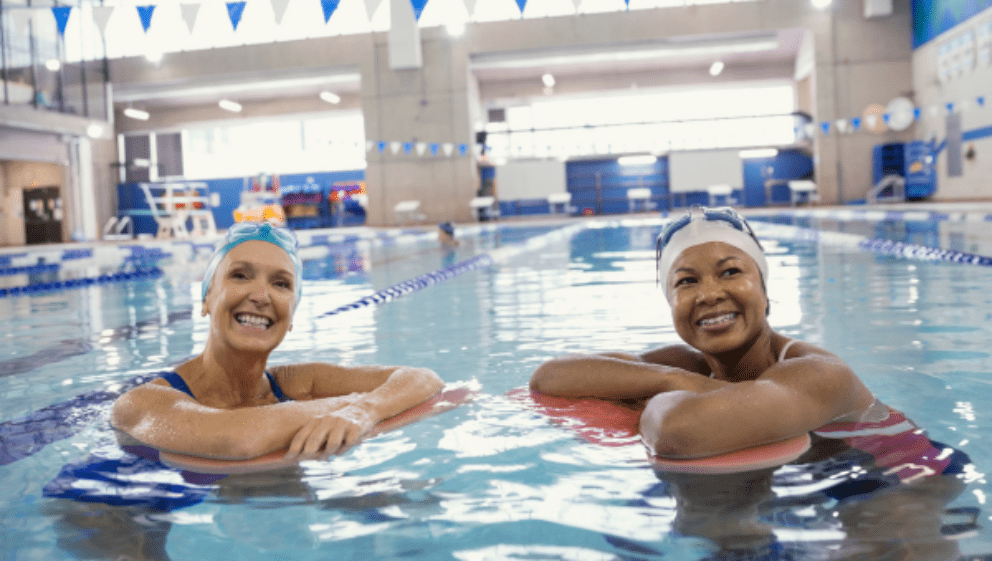 Swim 5k in March for Young Lives vs Cancer. Two women smiling, in a swimming pool with swimming hats.