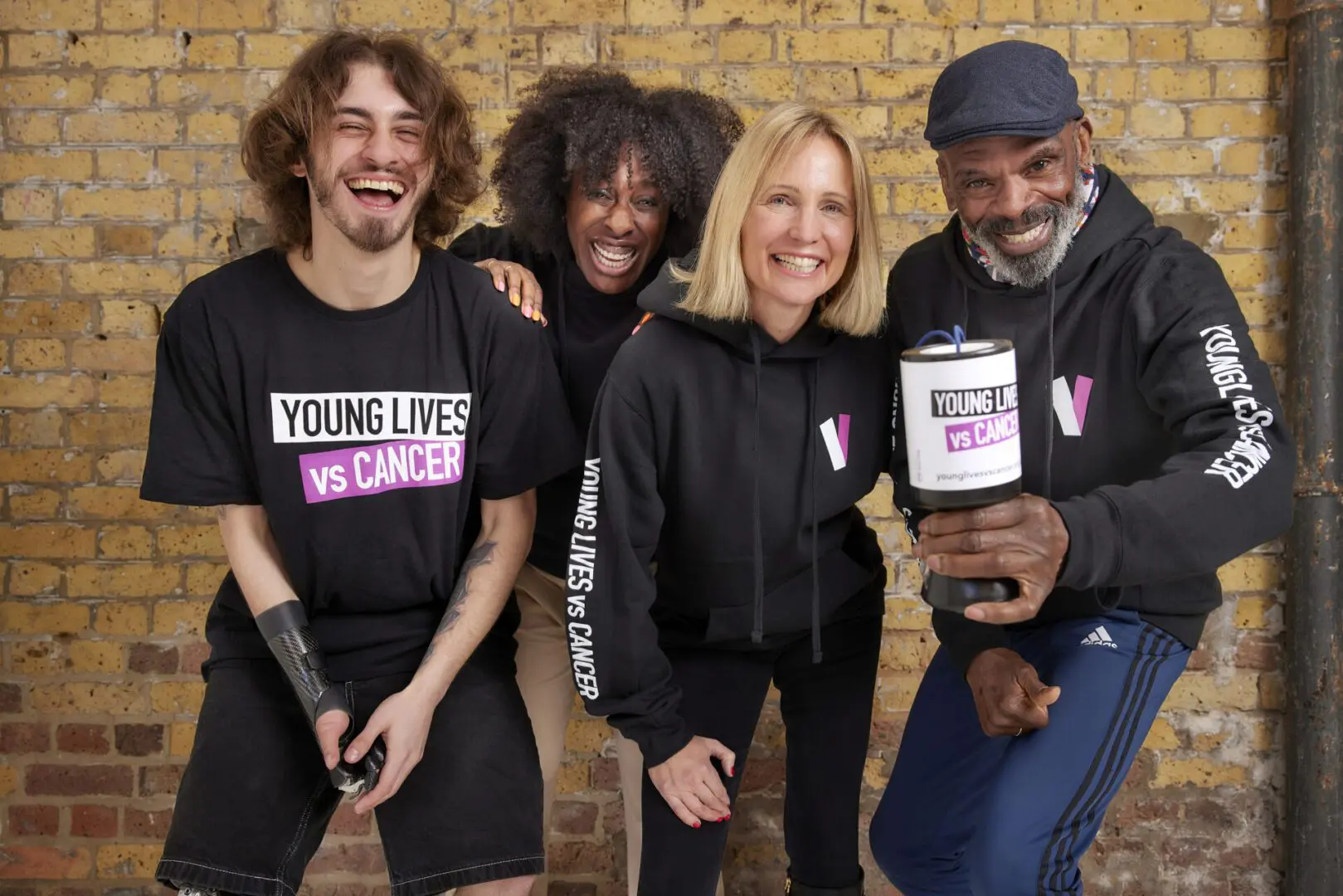 Four people stand together dressed in Young Lives vs Cancer clothing and one holds a collection pot.