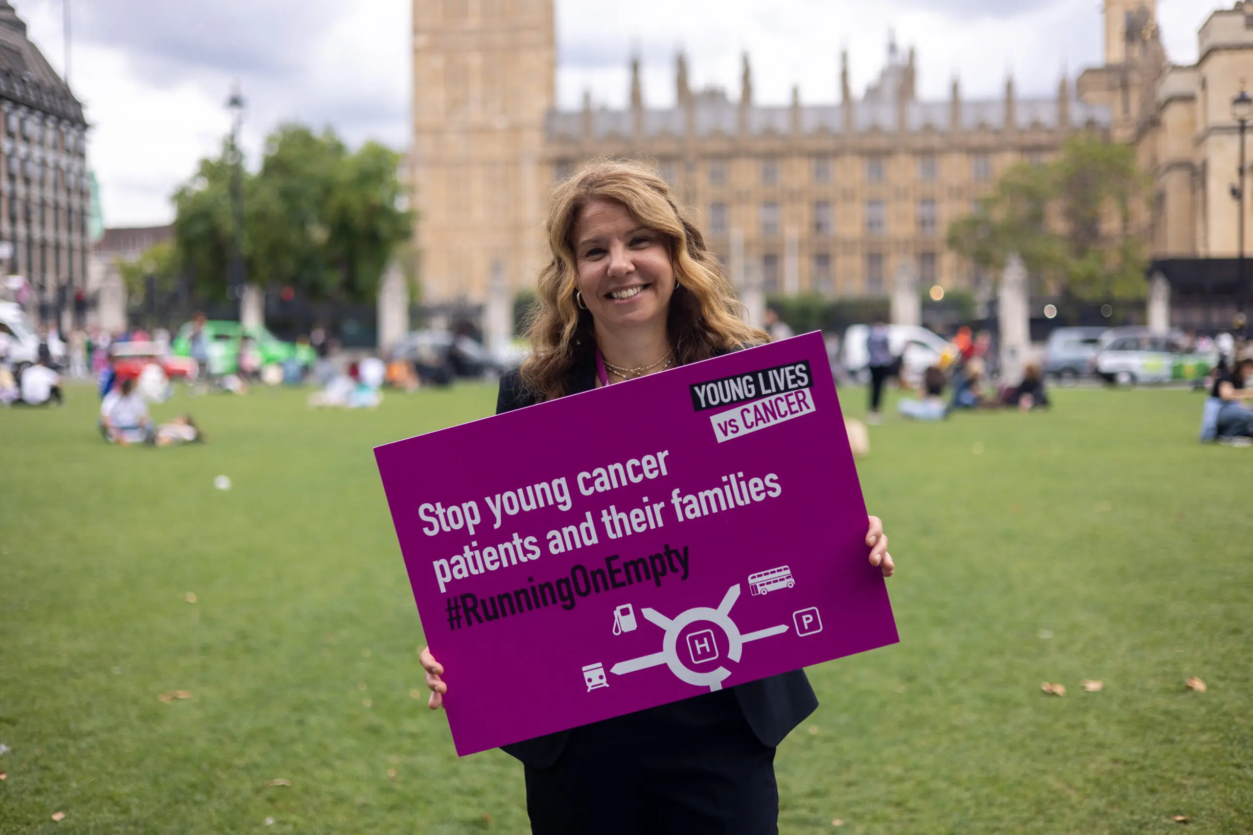 Rachel Kirby Rider Chief Exec at Young Lives vs Cancer holding a sign reading Stop young cancer patients and their families running on empty in parliament