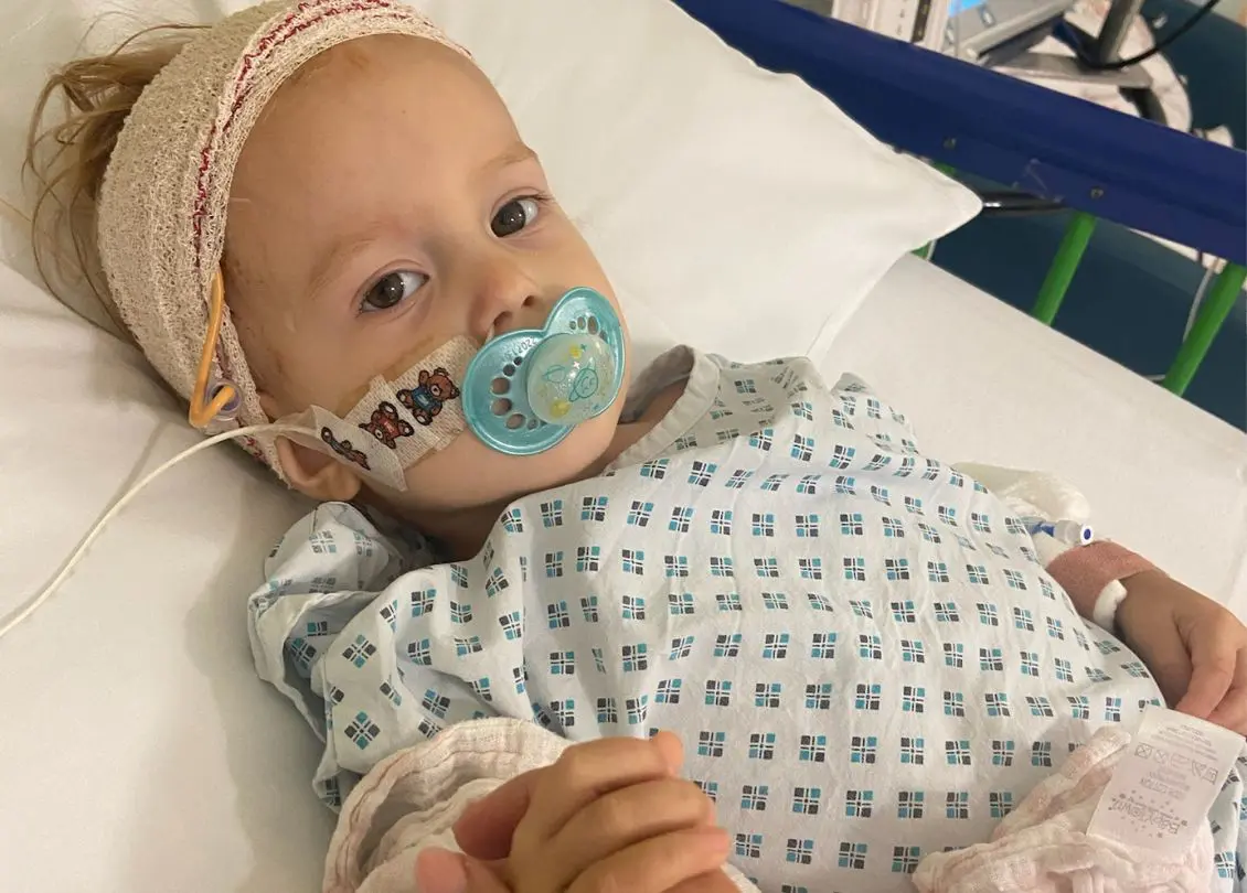 Little girl with a dummy - Orla - undergoing cancer treatment in hospital holding her parent's hand