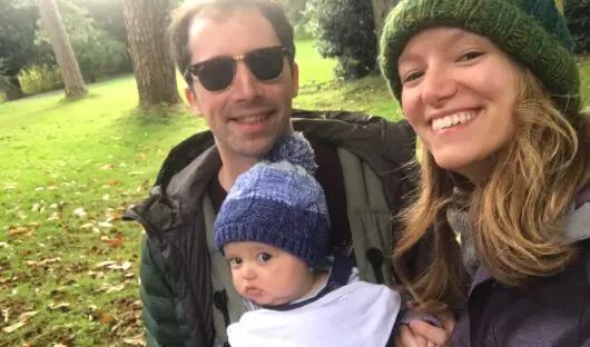 Amy and Matt with baby Rory. They are all smiling and wearing woolly hats and coats outside.