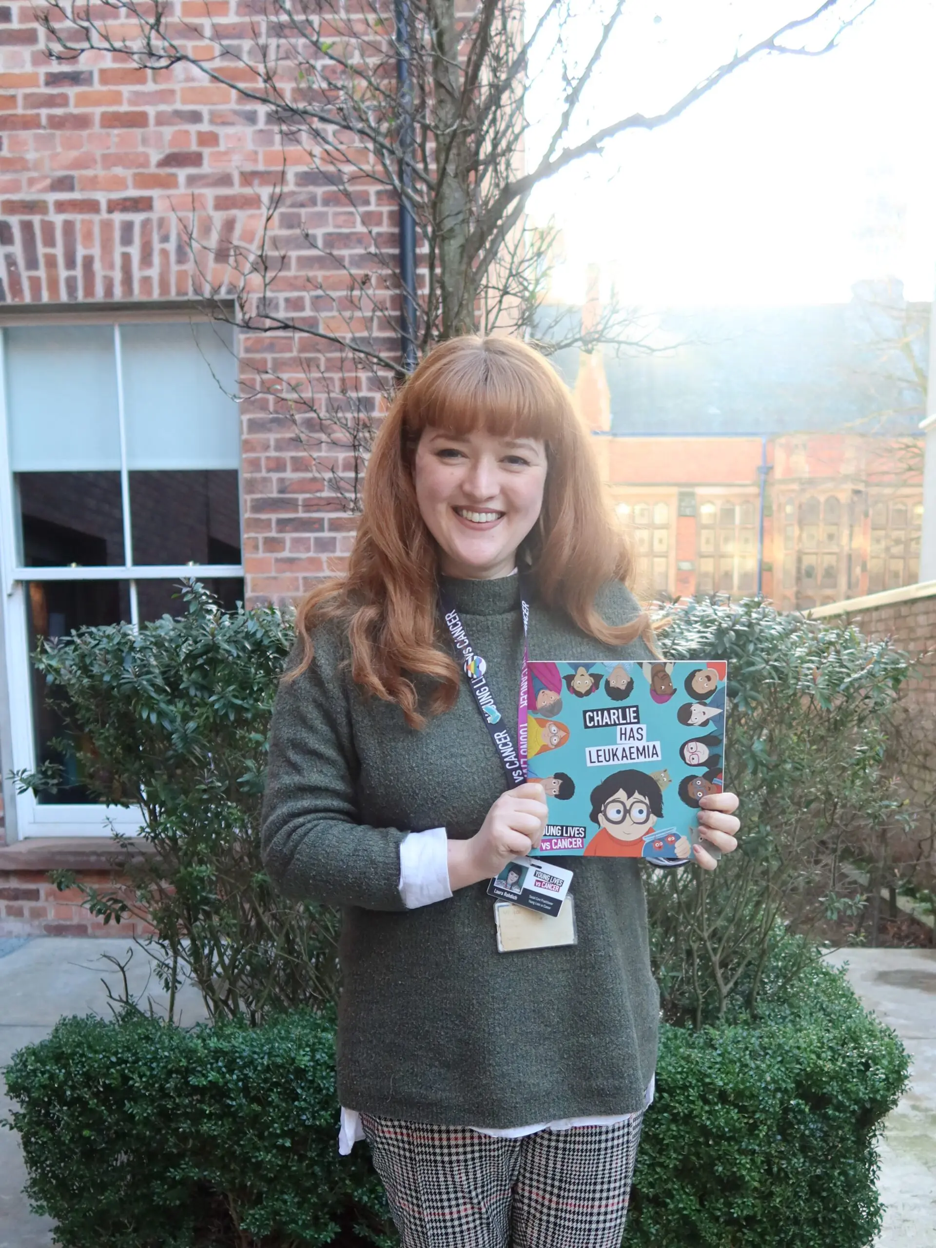 Young Lives vs Cancer Specialist Social Worker Laura is holding the updated storybook and smiling