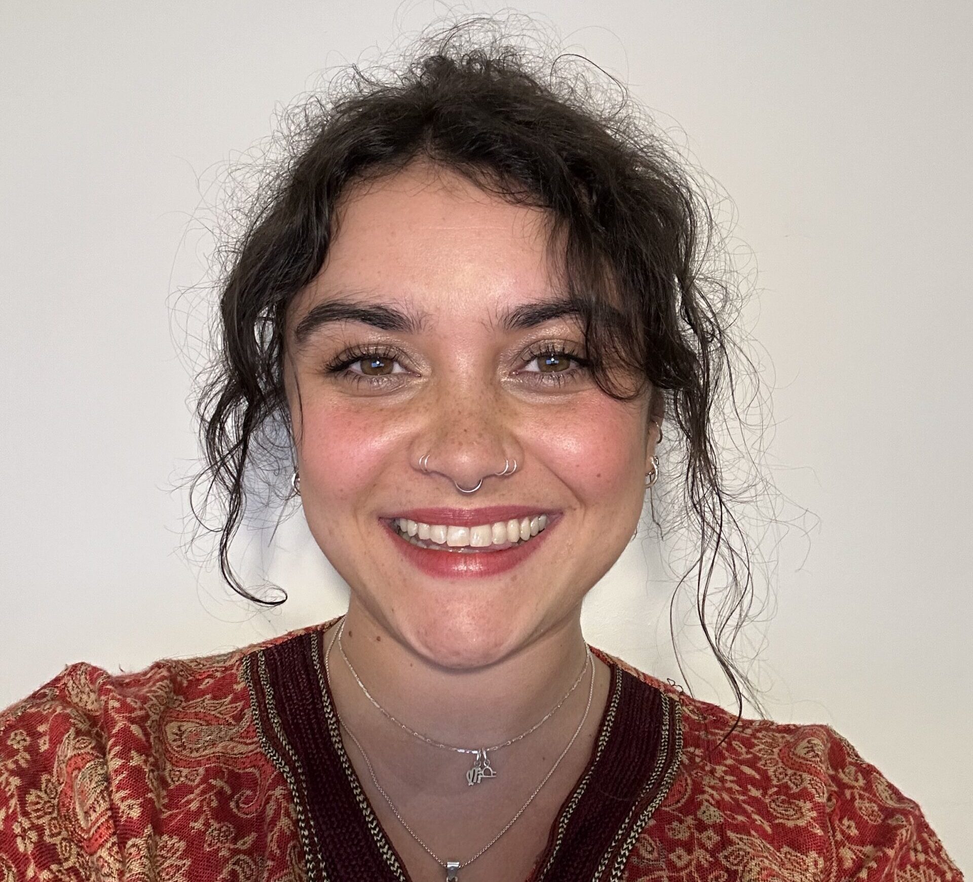 This is a selfie featuring a woman, Emma. She has curly brown hair and is wearing an orange top with yellow and brown patterns.